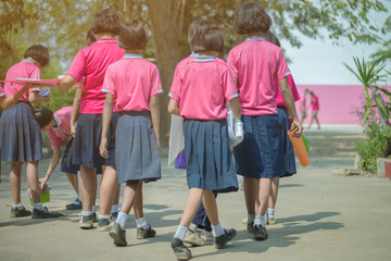 Fototapeta na wymiar Back view of happiness primary girl students in pink shirt and blue skirt walk to classrooms with their friends.
