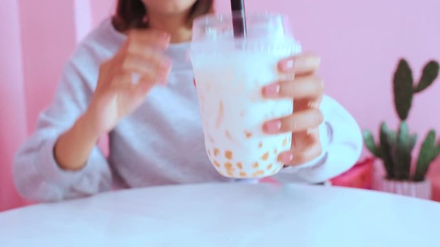 Young asian millennial woman drinking iced bubble milk tea in pink pastel cafe