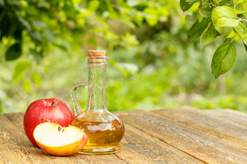 Apple vinegar in glass bottle and fresh red apples on wooden boards