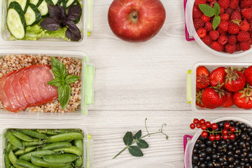 Apple and plastic meal prep containers with fresh berries, boiled buckwheat porridge and slices of meat, cucumbers and salad.