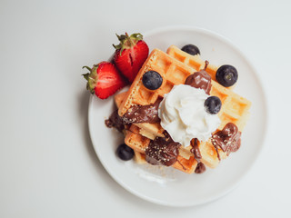 Breakfast flat lay. Tasty waffle with fruits, chocolate and whipped cream on a white ceramic plate