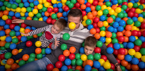 Fototapeta na wymiar dad and kids playing in pool with colorful balls
