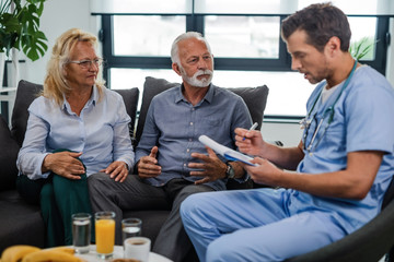 Senior husband and wife talking to healthcare worker at their home.