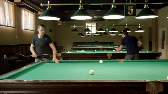 Men playing billiards, hitting the balls with a cue into pockets on a billiard table. 4K