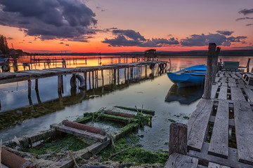 Fototapeta premium Exciting sunset on the harbor with wooden piers and boat. Horizontal view