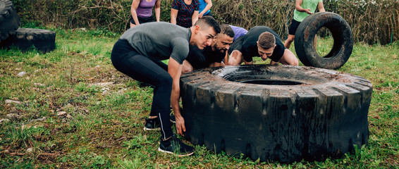 Group of participants in an obstacle course turning a truck wheel