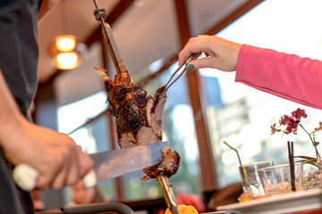 hands cut off meat from skewers at restaurant brunch
