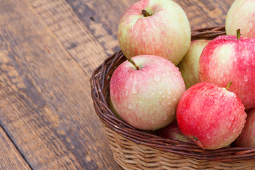 Red apples in wicker basket on old wooden boards