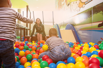 Fototapeta premium young mom playing with kids in pool with colorful balls