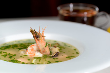 seafood soup in a white plate decorated with shrimps