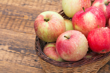 Red apples in wicker basket on old wooden boards