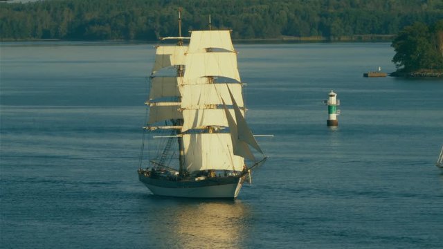 A majestic two-masted tall ship sails upstream to return to port after cruising the ocean.