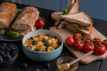 Food. Breakfast. Meal. Snack. Sandwich, baguette, toast. Corn flakes on black background. Fresh delicious food set. Traditional lunch