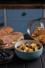 Meal. Kitchen. Food. Delicious breakfast. Sandwich with salad, baguette with tomato and bowl of cornflakes with fruit and honey on black table