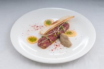 veal tartare with pate and microgreen on a white plate on a pure white background