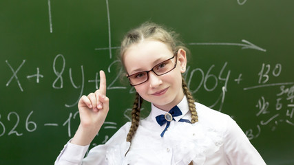 Funny schoolgirl with glasses with thick lenses. Student teenager in big glasses for poor vision raised up the index finger I have an idea