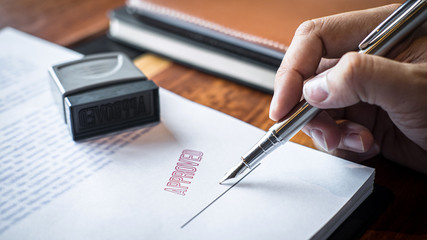 Close up hands of businessman signing and stamp on paper document to approve business investment...