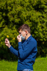 a man in a mask from allergy, in a blue shirt, stands in the park