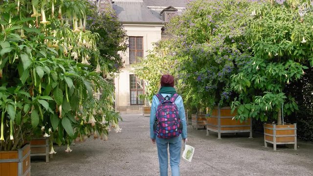 Hannover, Germany. A young female tourist with a map in her hands and a backpack walks around the aquarium with unusual trees that grow in huge wooden vases on which flowers grow. Looks