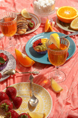 Appetizing breakfast, orange, croissant, strawberries and cakes on a red tablecloth. Top view.