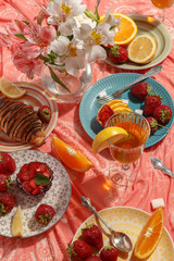 Fototapeta na wymiar Appetizing breakfast, orange, croissant, strawberries and cakes on a red tablecloth. Top view.
