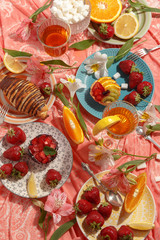 Appetizing breakfast, orange, croissant, strawberries and cakes on a red tablecloth. Top view.