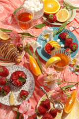 Appetizing breakfast, orange, croissant, strawberries and cakes on a red tablecloth. Top view.