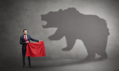 Businessman standing with red cloth in his hand and big bear shadow on his background
