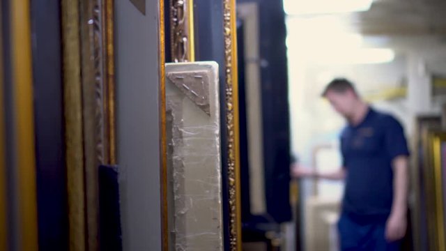Art frames standing in a row in storage and man on background counting frames