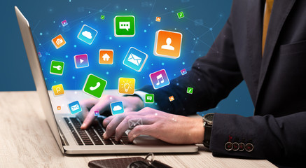 Businessman hand typing on laptop with flying application icons around
