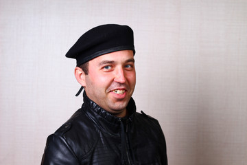 Cool rocker in black leather jacket smiling on blurred background wall in studio. Emotion of...