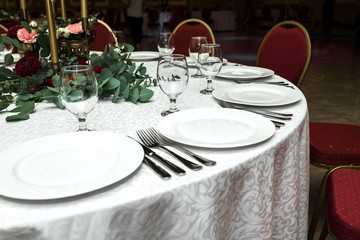 Festively decorated round banquet table in the restaurant. Fresh flowers are golden candles and red chairs. expensively rich