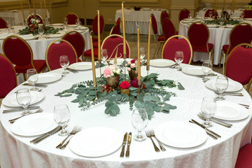 Festively decorated round banquet table in the restaurant. Fresh flowers are golden candles and red chairs. expensively rich