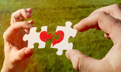 Two puzzles with a heart in his hands on a background of green grass. love, date.