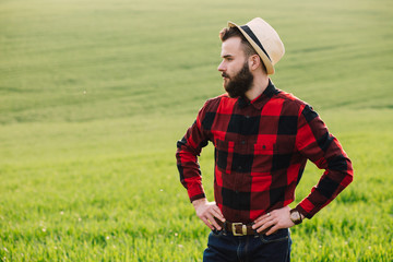 Young bearded agronomist standing in cultivated wheat crops field