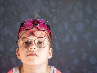 Photo of funny boy, blonde kid with  lot of pairs of glasses on his face. Child is happy at home on vacation.