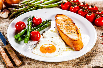Fried egg with vegetables and toast on wooden table