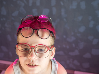 Fototapeta na wymiar Photo of funny boy, blonde kid with lot of pairs of glasses on his face. Child is happy at home on vacation.