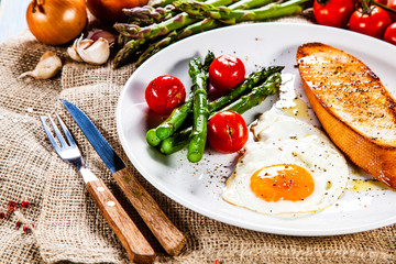 Fried egg with vegetables and toast on wooden table