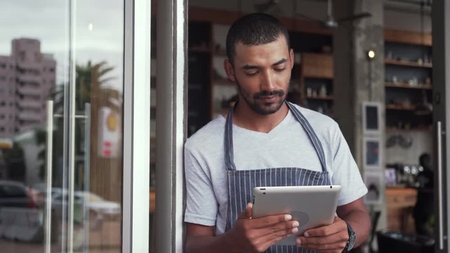 Male owner standing at the doorway of his cafe holding digital tablet