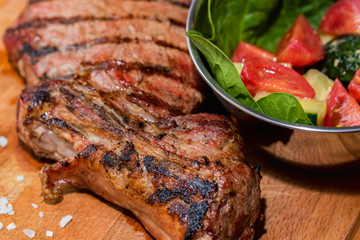 Close up freshly grilled bone steak on wood and fresh salad in bowl