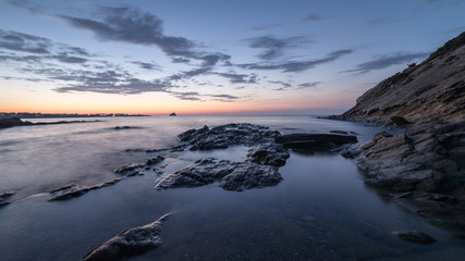 Rocks above the a quiet sea in long exposure under a cloudy sky at sunrise