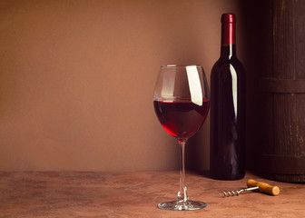 A glass of red wine and a bottle on dark background. Copy space. Still life style dark. Selective focus.