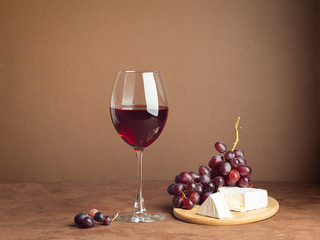 A glass of wine a bunch of red grape cheese slice dark background. Copy space. Still life style...