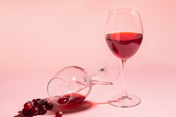A glass of red wine on the table is turned upside down and a bunch of grapes on gentle pink...