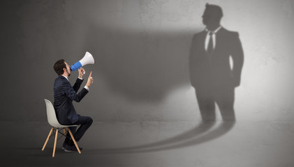 Humble businessman staying and offering stuffs to a huge businessman shadow

