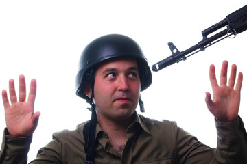 A man in a military helmet with raised hands looks at the muzzle of a rifle aimed at his face....