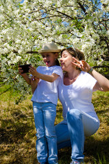 Mom and daughter together. Do selfie on the phone. Background summer nature.