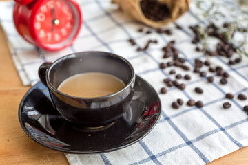 Coffee in a black coffee cup Placed on a fabric with coffee beans and morning alarm clocks.