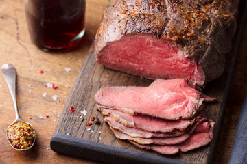 Roast beef on cutting board with glass of wine. Wooden background. Close up.